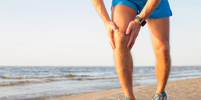 A man with an aching knee while running on the beach