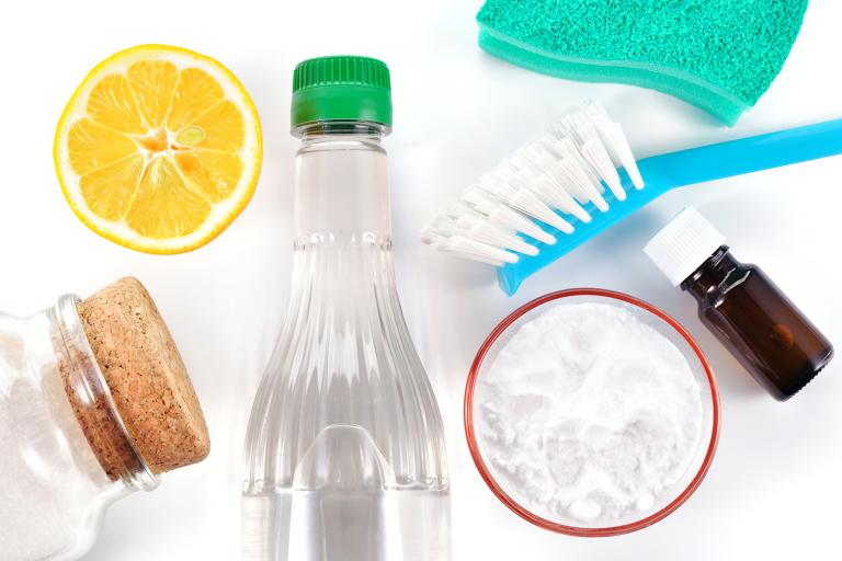 a sponge, a brush, vinegar, a lemon, baking soda, and a bottle of essential oil