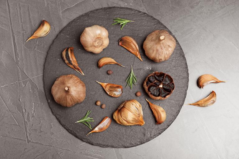 Slate plate with aged black garlic and rosemary on gray background, top view.